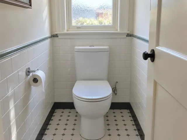 Clean white toilet in a small tiled bathroom with a window and patterned floor in Concord