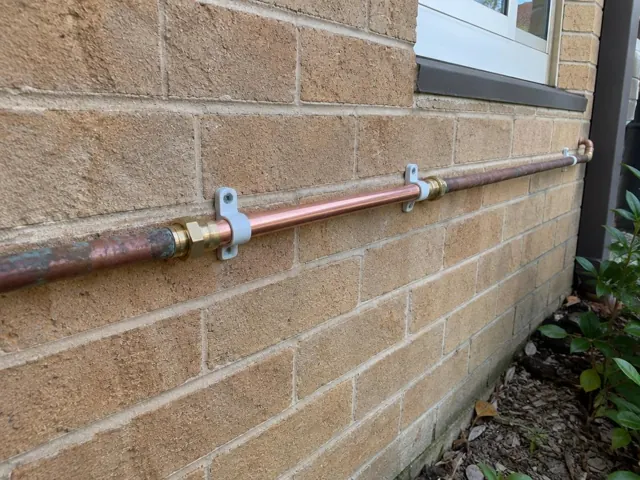 Repaired copper water pipe on a brick exterior wall in a narrow side yard in Mortlake