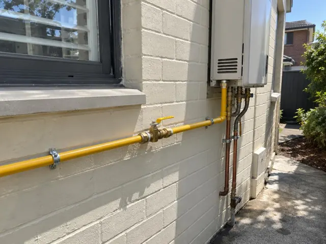 Yellow gas piping and wall-mounted appliance on exterior brick wall in Rhodes